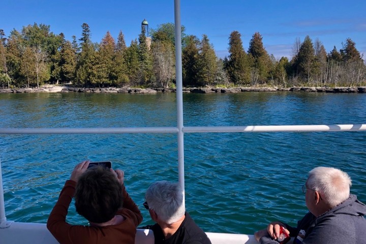 a group of people on a tour boat in baileys harbor viewing the birdcage lighthouse