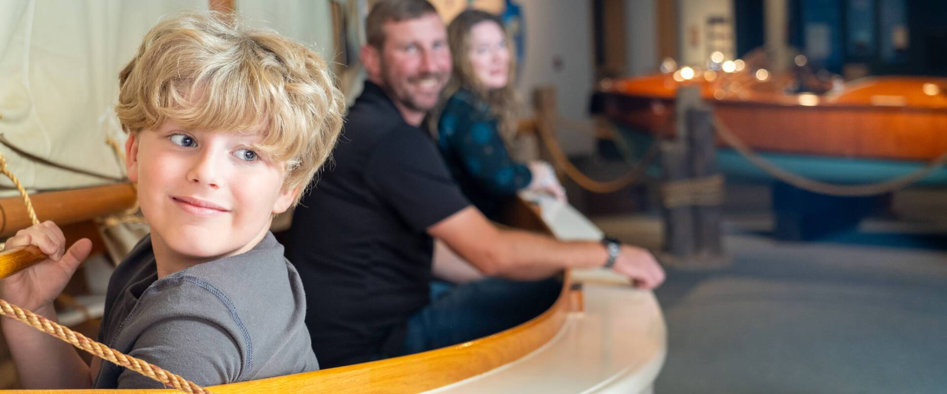 a little boy and parents sitting inside a boat in an exhibit gallery of Wisconsin Maritime Museum
