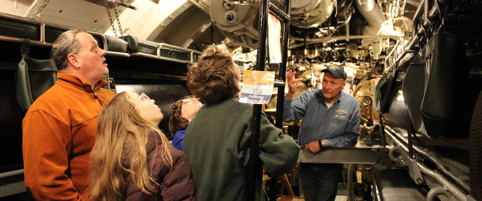 A family and a museum staff standing inside a ship mechanical area at Wisconsin Maritime Museum