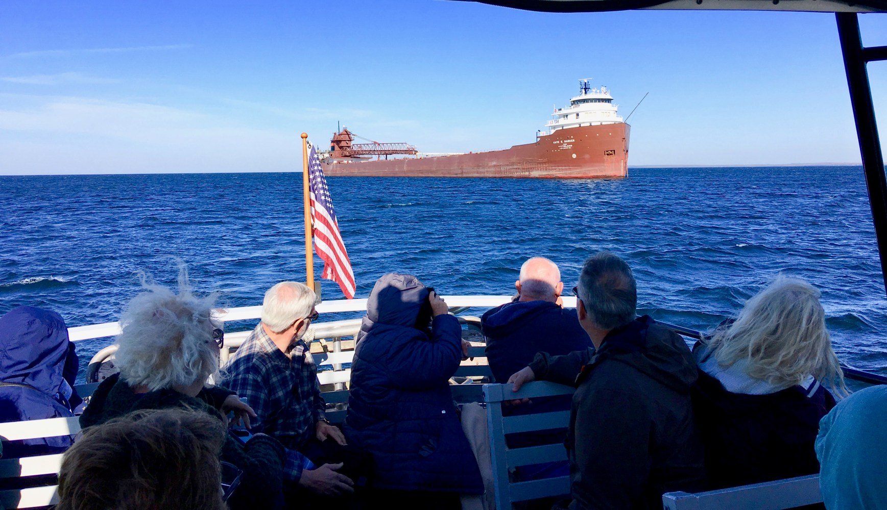 a group of people sitting in a boat on a body of water looking at a large freighter