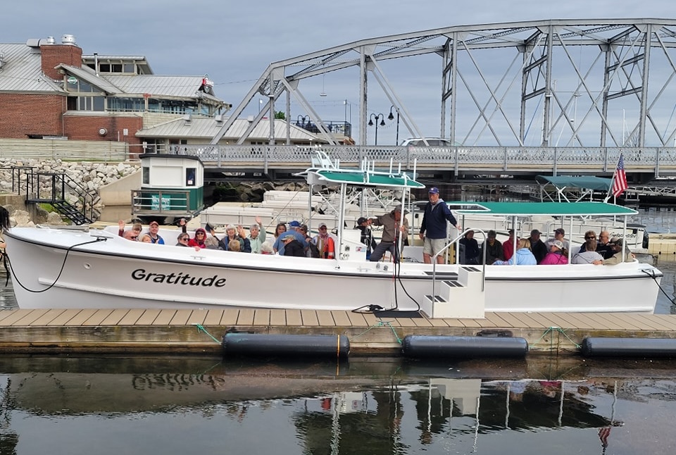 Guests full boat Gratitude a tour boat full of people is docked next to a body of water and a bridge