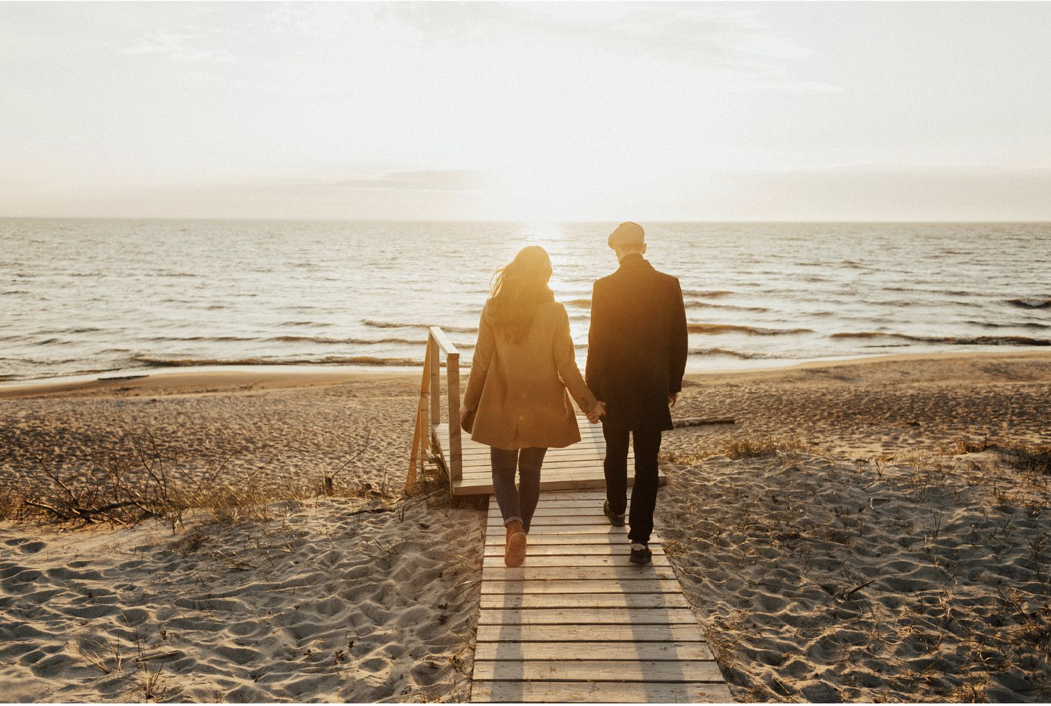 couple a couple walking on a boardwalk toward a body of water