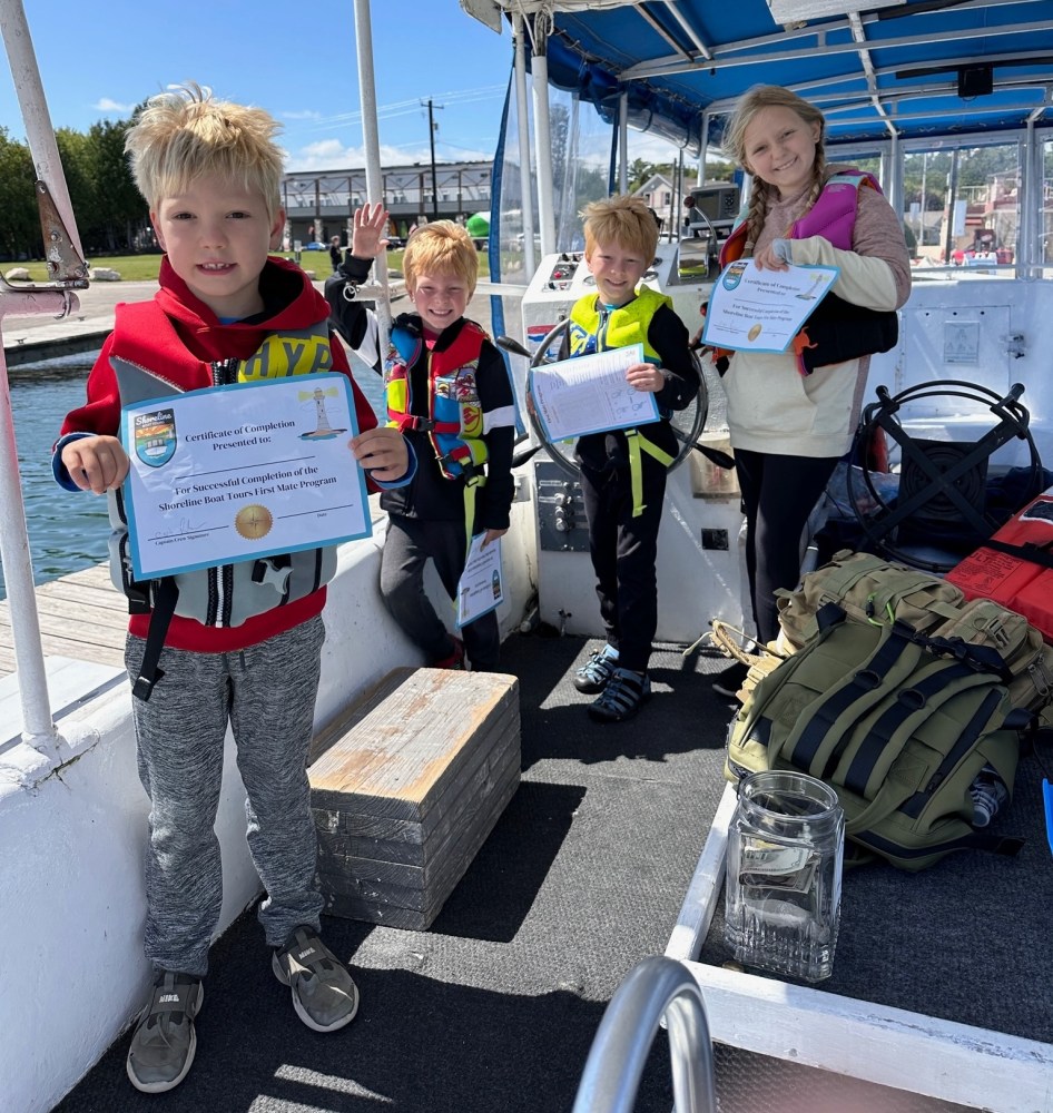 Four children on a boat holding completion certificates and wearing life jackets.