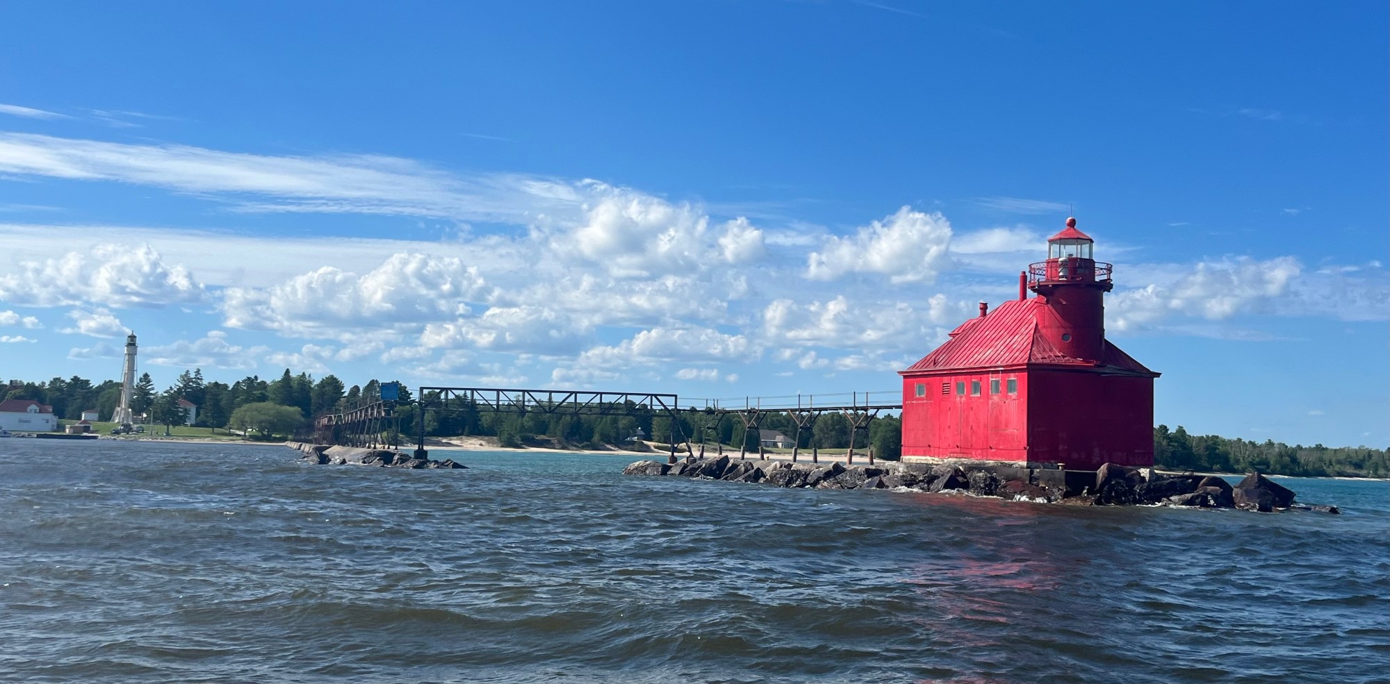 Pierhead IMG_6135 Red lighthouse on rocky shore with bridge and blue sky in background.