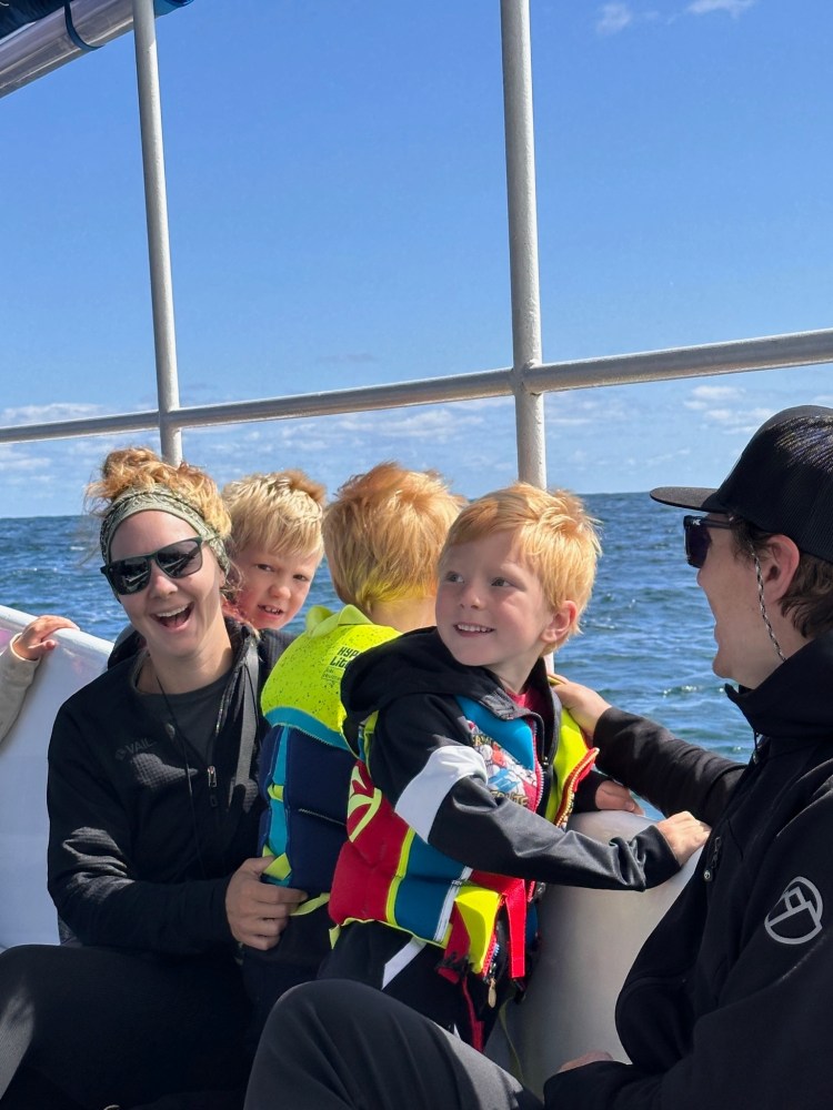 Group of people on a boat, two kids in life vests, blue ocean and sky in the background.