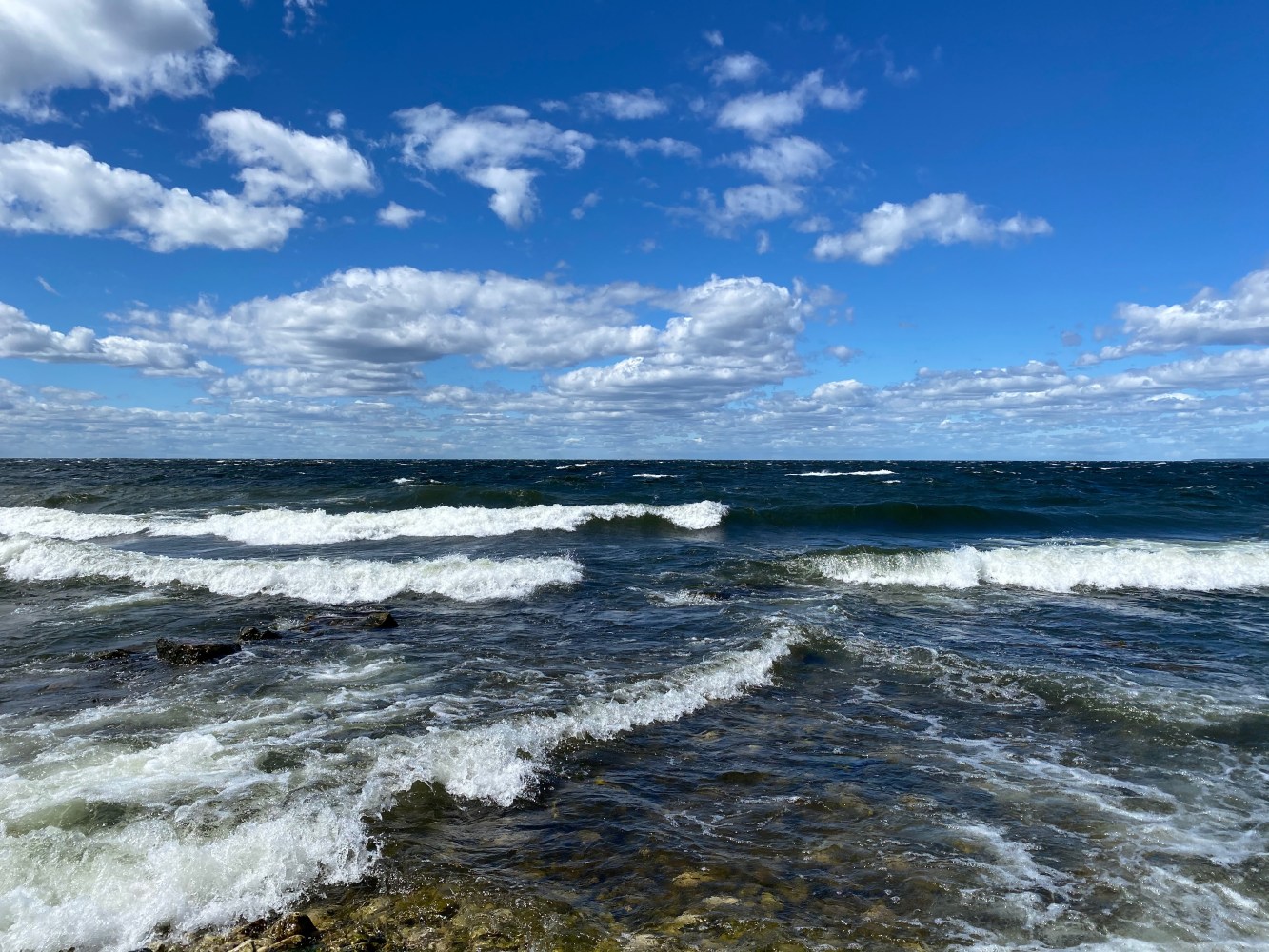 Ocean waves under a blue sky with scattered clouds.