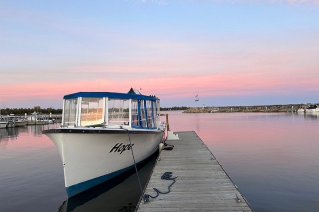 Boat docked at a pier with pink sunset sky over calm water.