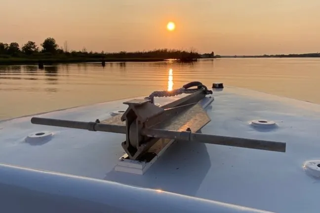 Boat deck view facing sunset over calm water with distant trees.