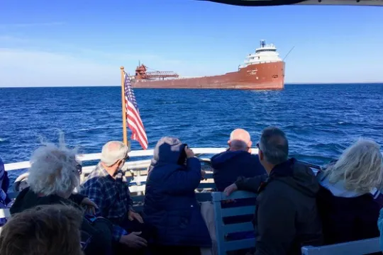 A group on a boat watches a large cargo ship with American flag visible on open sea.