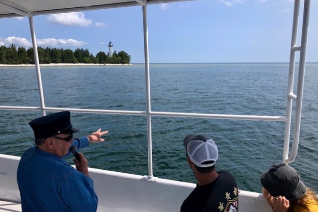 People on boat looking at distant lighthouse on shoreline under clear sky.