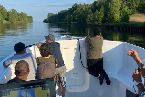 People on a boat looking at waterway surrounded by trees.