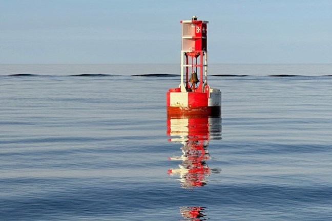 Red buoy with number 8, floating on calm blue sea under clear sky.